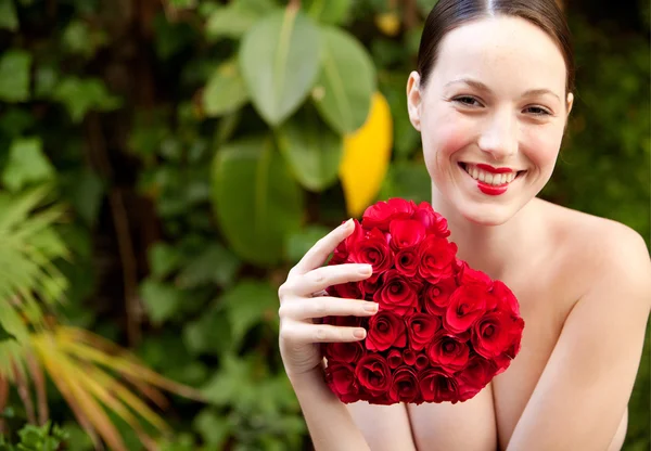 Nude girl holding a red roses heart in a garden — Stok fotoğraf