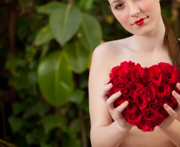 Nude girl holding a red roses heart in a garden 图库照片