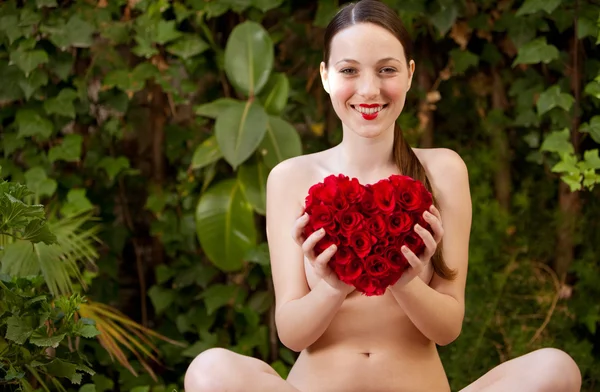 Menina nua segurando um coração de rosas vermelhas em um jardim Imagem De Stock