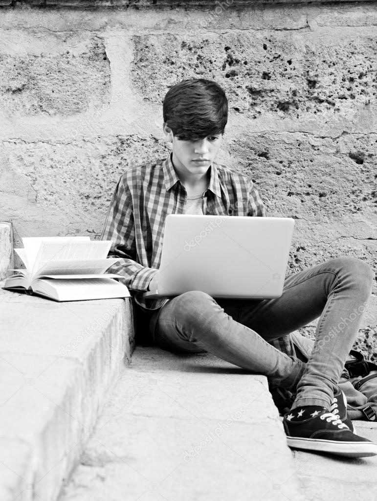 boy with school books and a laptop computer outdoors