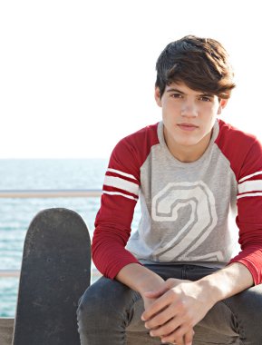 boy sitting on a bench by the sea with his skateboard