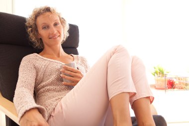 woman drinking a hot beverage in a armchair clipart