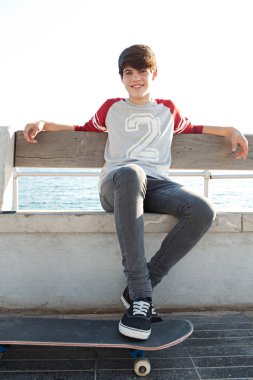 boy with a skateboard and sitting down on a bench by the sea