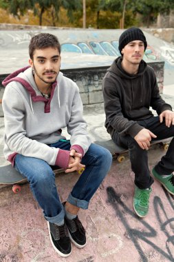 two teenagers friends sitting at a skateboarding park