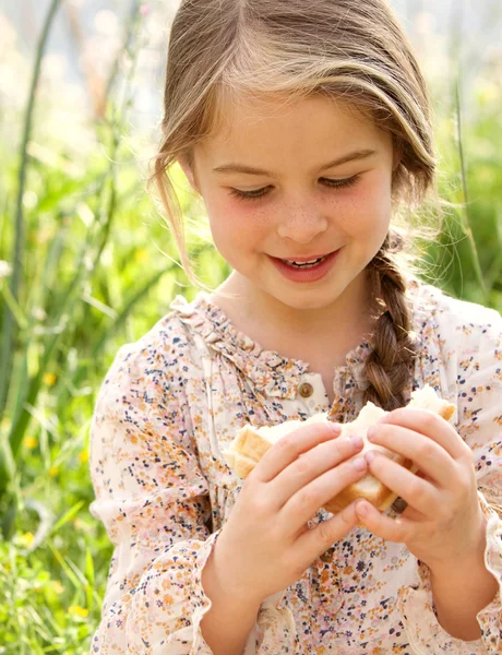 Девушка ест свежий сэндвич в поле — стоковое фото
