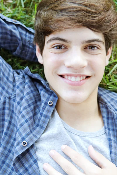 Smiling boy laying down on green grass in a park — Stock fotografie