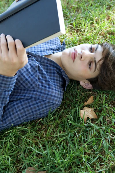 Tiener jongen lezen van een boek op gras — Stockfoto