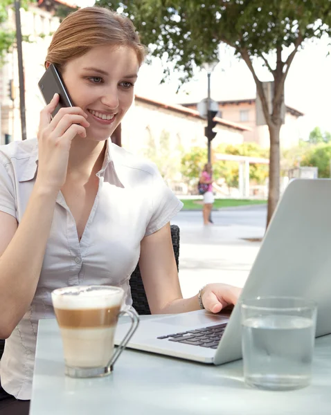 Mujer de negocios que usa una computadora portátil mientras está en una llamada telefónica en la cafetería —  Fotos de Stock