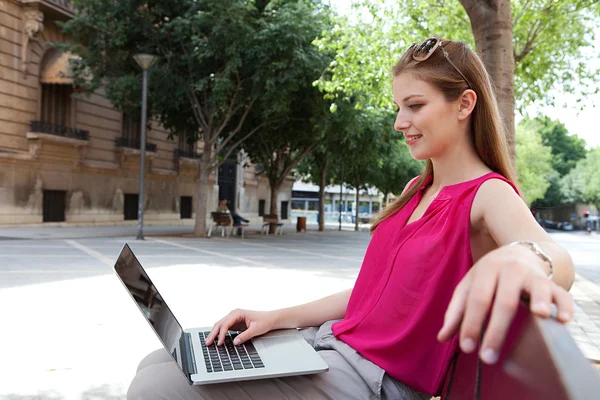 Business woman working on her laptop computer while relaxing on a wooden bench — Stockfoto