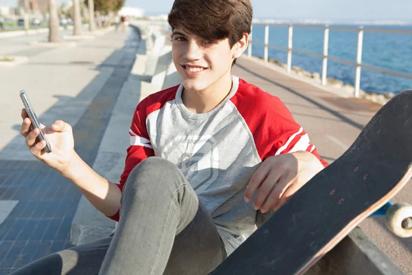 Boy with a skateboard using a smartphone — Stock Fotó