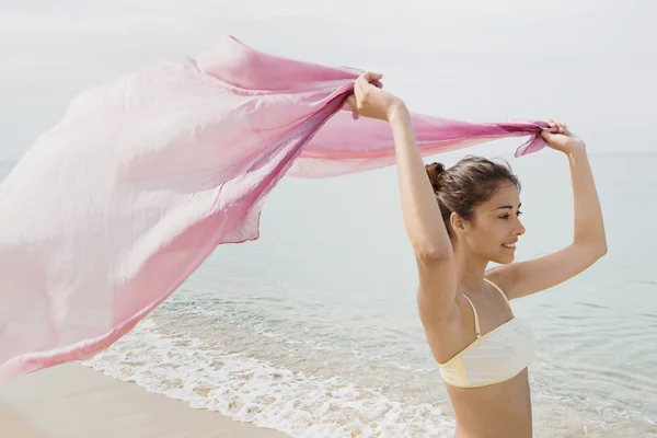 Jovem mulher com um sarong tecido rosa na praia — Fotografia de Stock