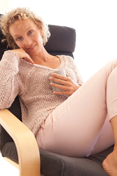 Woman drinking a hot beverage in a armchair — Stok fotoğraf