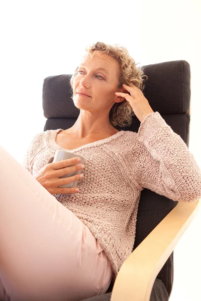 Woman drinking a hot beverage in a armchair — Stockfoto