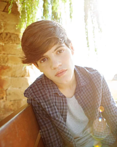 Attractive teenager boy sittingon a wooden bench — Stock Fotó