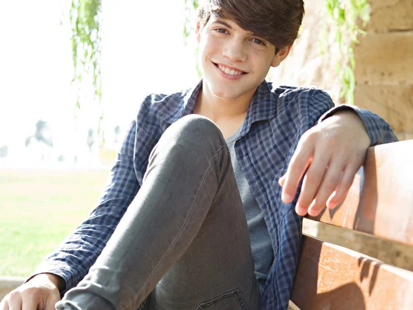 Boy sitting on a wooden bench in a park — Φωτογραφία Αρχείου
