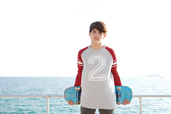 Мальчик, стоящий у моря со скейтбордом — стоковое фото