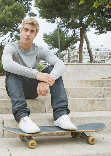 Uomo seduto nel parco con il suo skating board — Foto Stock