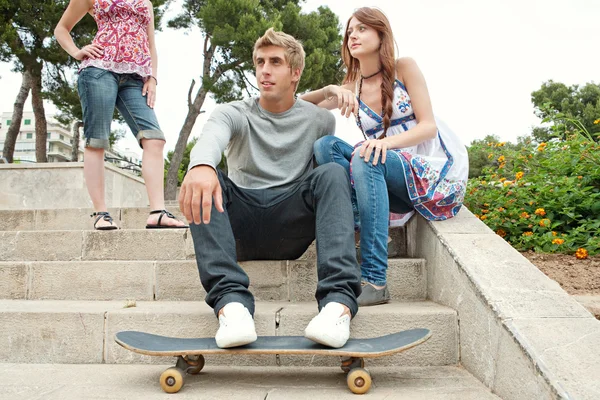 Friends sitting on stone steps with a skating board — Stok fotoğraf