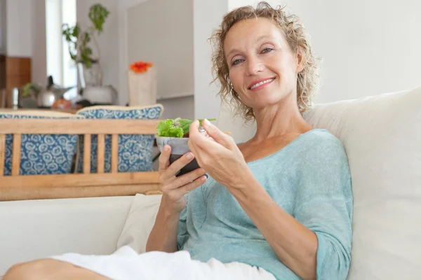 Frau isst Salat auf der Couch zu Hause — Stockfoto