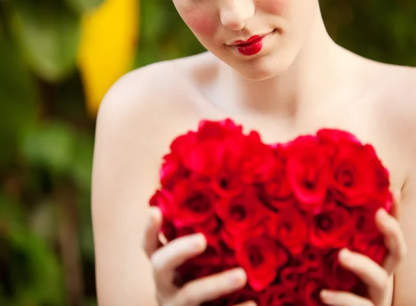 Chica desnuda sosteniendo un corazón de rosas rojas en un jardín — Foto de Stock