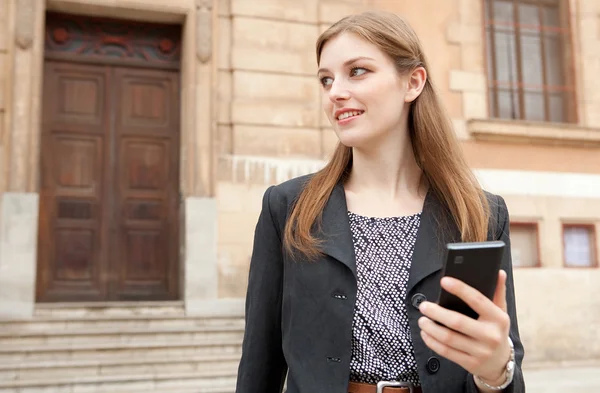 Бізнес-леді посміхається і використовує смартфон — стокове фото