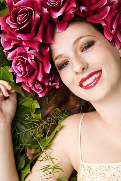 Mulher deitada em uma floresta usando um vestido de cabeça de rosas vermelhas — Fotografia de Stock
