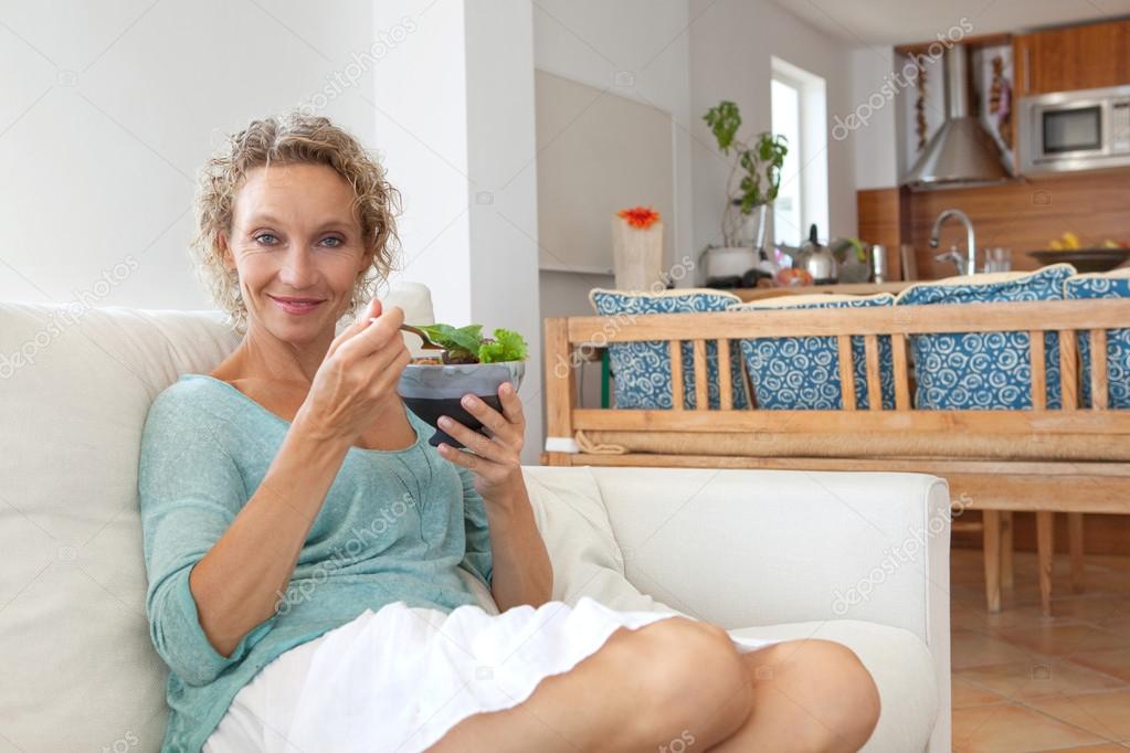 woman eating a salad on a couch at home