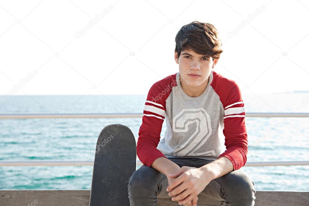 boy sitting on a bench by the sea with his skateboard