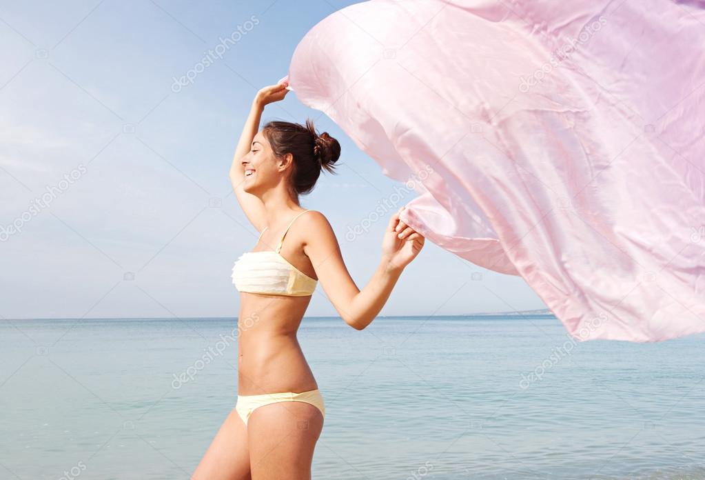 woman on a beach holding up a pink fabric