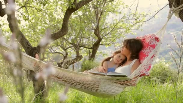 Moeder en dochter lezen van een boek in een hangmat — Stockvideo