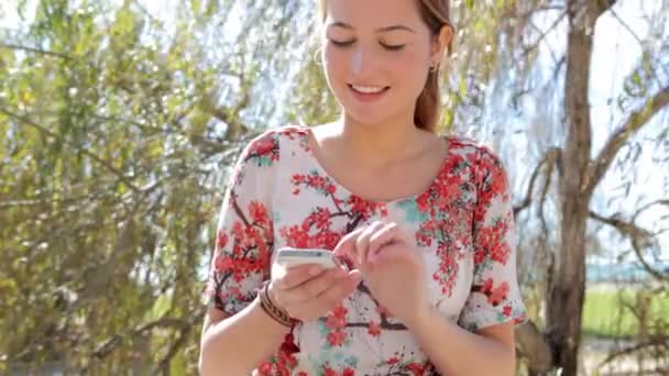 Vrouw met behulp van een slimme telefoon zittend in een park — Stockvideo