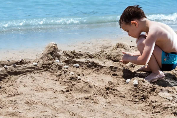 Niño en el mar azul jugando con pasteles de barro y arena — Foto de Stock