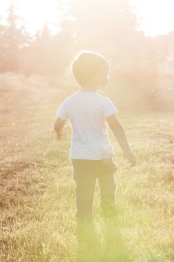 Yalnız küçük bir çocuk gün batımında toprak yolda yürüme