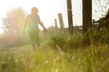 Yalnız küçük bir çocuk ahşap çit boyunca günbatımı bir kir yolda yürürken