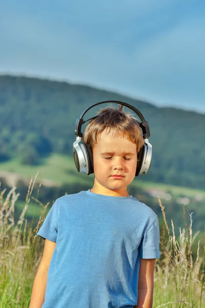 Cute 6 year old boy listening to music on headphones in nature — Stock Photo, Image