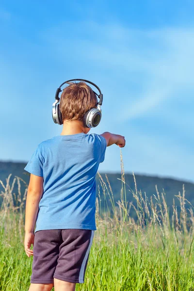 Bonito menino de 6 anos ouvindo música em fones de ouvido na natureza — Fotografia de Stock