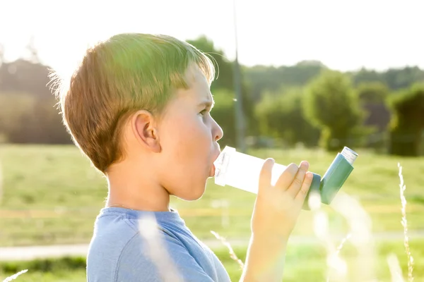 Niño usando inhalador para el asma en la aldea con puesta de sol de verano —  Fotos de Stock