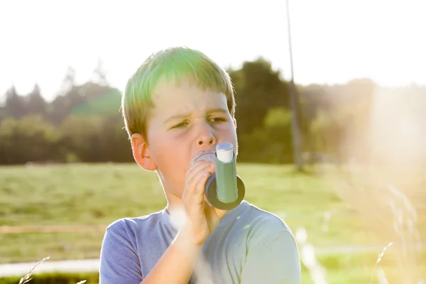 Niño usando inhalador para el asma en la aldea con puesta de sol de verano —  Fotos de Stock