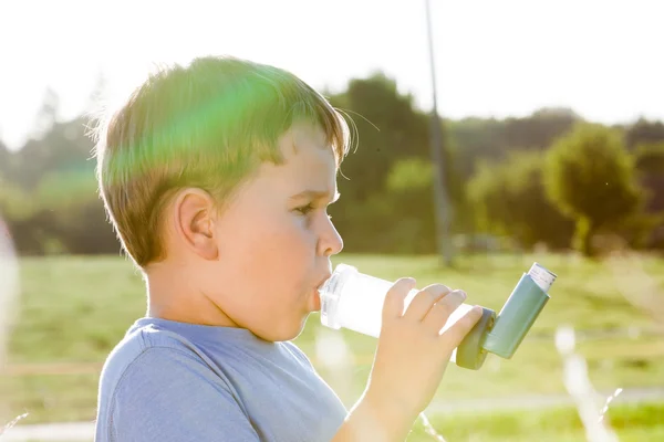 Niño usando inhalador para el asma en la aldea con puesta de sol de verano — Foto de Stock