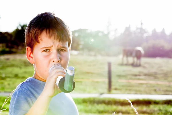Niño usando inhalador para el asma en la aldea con puesta de sol de verano — Foto de Stock