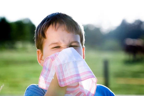 Criança com alergia ao pólen enquanto assoa o nariz com um lenço branco na natureza — Fotografia de Stock