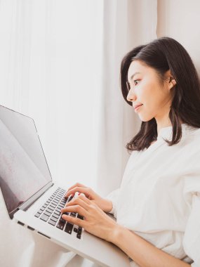 Genç Asyalı kadın evde bilgisayar kullanıyor.