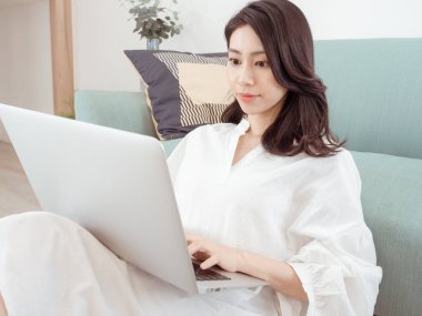 Genç Asyalı kadın evde dizüstü bilgisayar kullanıyor.