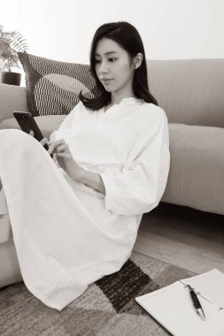 Genç Asyalı kadın evde akıllı telefon kullanıyor.