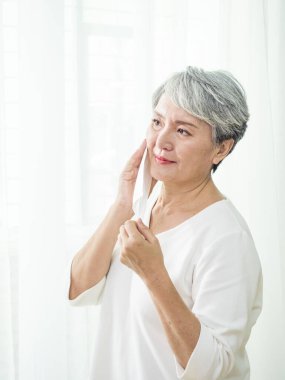 Koronavirüs ve grip salgını sırasında maske takan son sınıf Asyalı kadın. Virüs ve hastalık koruması, ev karantinası. COVID-2019. Maskeleri çıkarmak ya da çıkarmak.