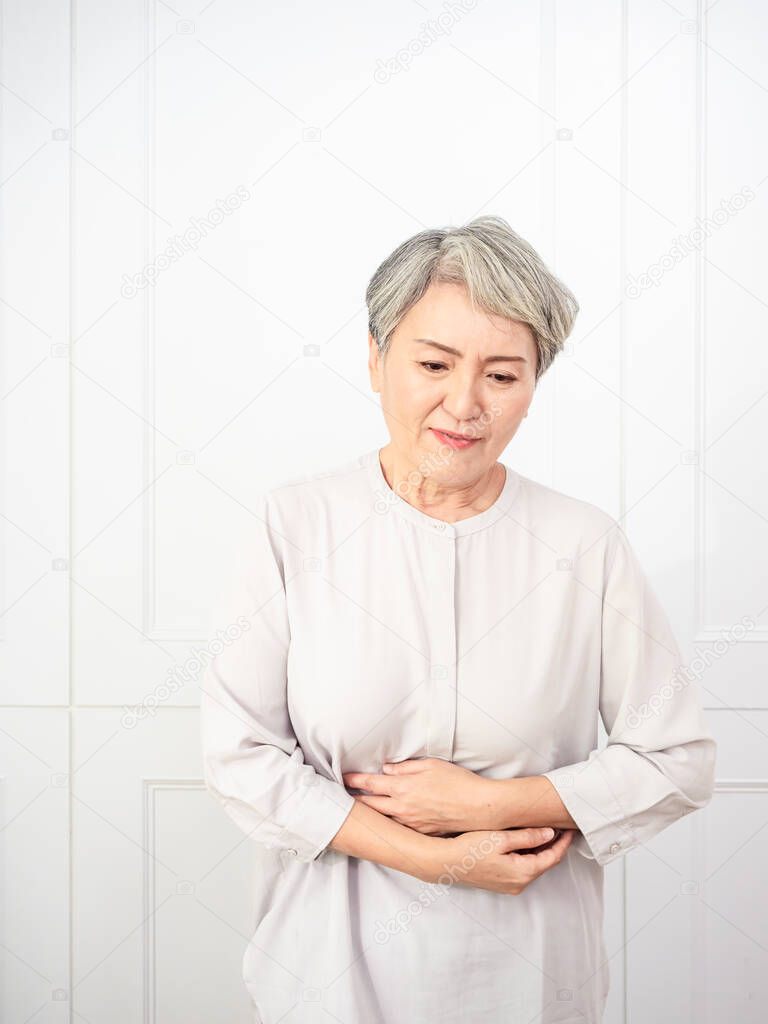 Senior asian woman wearing casual clothes with hand on stomach because indigestion, painful illness feeling unwell. ache concept.