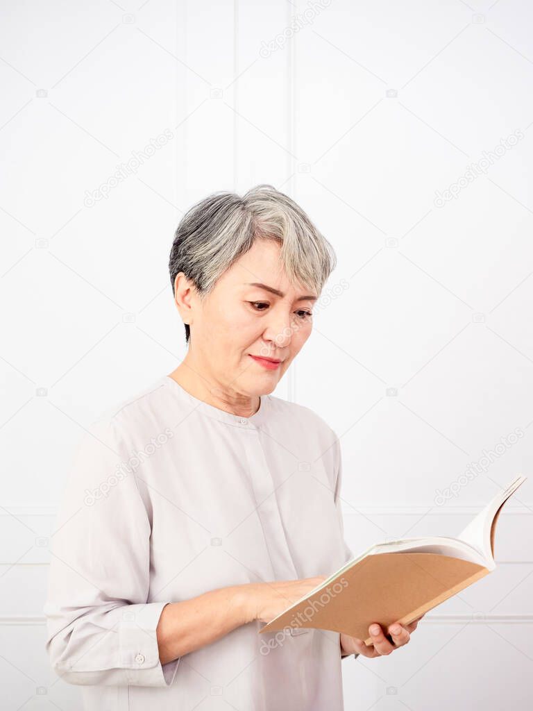 Senior grey hair Asian woman holding and reading book at home.