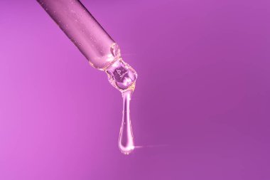 Pipetten bir damla serum ve ışıktan önemli noktalar. Parlak mor bir arkaplanda.
