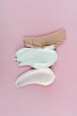 Açık pembe arka planda farklı kozmetik lekeler. Yukarıdan görüntüle.