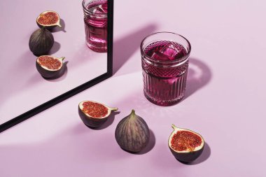 İncirlerle süslenmiş renkli bir kokteyl. İncirlerle süslenmiş mor kokteyl rengi, ön manzara. Pembe bir arka planda